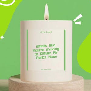 May include: A white cylindrical soy wax candle in a glass container with a lit wick. The label features the text Lime Light and Smells like You're Moving to Offutt Air Force Base, with soy wax 9 oz printed at the bottom in green lettering.