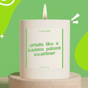May include: A white cylindrical soy wax candle with a lit wick. The label features the text Lime Light, Smells like a badass patent examiner, and soy wax | 9 oz in green lettering, framed by two vertical green lines on a white background.