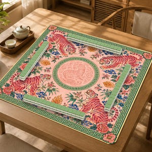 May include: A square mahjong mat featuring a pink background with four tigers, colorful floral patterns, and a central circular tiger motif. The mat is bordered by a green geometric pattern and includes four rows of light green mahjong tiles.
