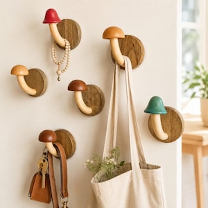 May include: A collection of six wall-mounted mushroom-shaped hooks, each featuring a circular wooden base and a curved stem. The mushroom caps are painted in various colors including red, brown, and green, used to hang items like bags and keys.