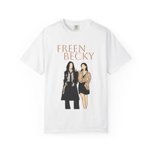 Puede incluir: Una camiseta blanca de manga corta con una ilustración gráfica de dos figuras de pie una al lado de la otra. Sobre la ilustración, el texto FREEN BECKY está impreso en una fuente serif marrón. Las figuras están en un estilo de arte lineal.
