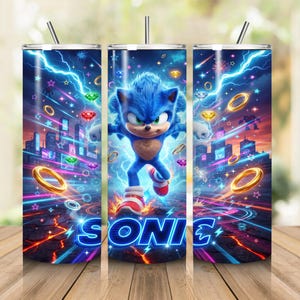 May include: A cylindrical tumbler featuring a vibrant graphic of the blue character Sonic running through a neon city landscape. The design includes golden rings, colorful gemstones, and lightning bolts, with the word SONIC printed in bold blue letters.