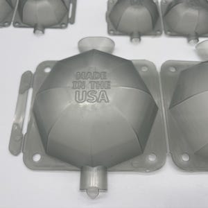 May include: A close-up of a gray plastic mold with a hexagonal shape. The mold has a raised design and the text "MADE IN THE USA" is printed on the surface.