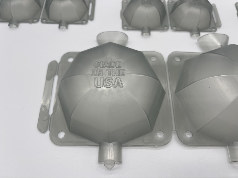 May include: A close-up of a gray plastic mold with a hexagonal shape. The mold has a raised design and the text "MADE IN THE USA" is printed on the surface.