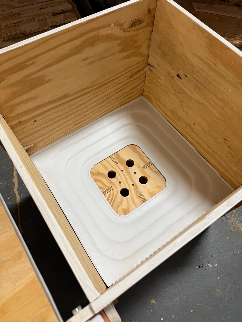 Pu&ograve; includere: Una scatola di legno con interno bianco e base quadrata in legno con quattro fori. La scatola &egrave; costruita in compensato di colore chiaro e ha un aspetto pulito e non rifinito. L'interno bianco ha un design a gradini.