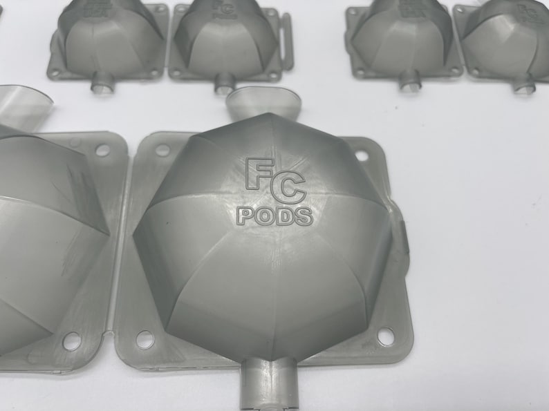 May include: A close-up of a gray plastic mold with the text "FC PODS" printed on the top. The mold is designed to create small, round objects.