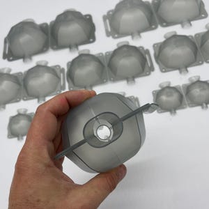 May include: A collection of gray plastic molds, some are in a hand, all are in the shape of a dome with a hole in the center.