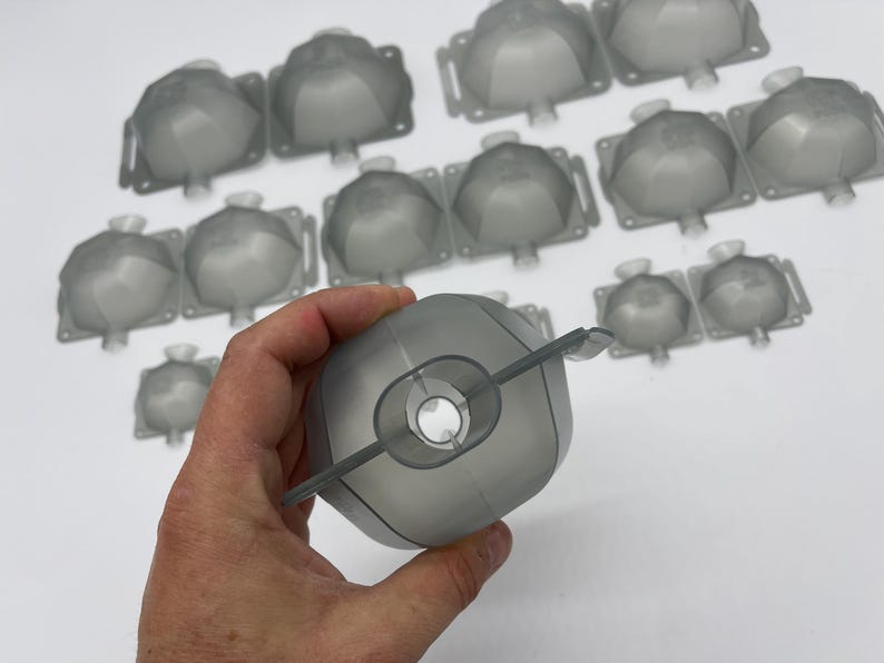 May include: A collection of gray plastic molds, some are in a hand, all are in the shape of a dome with a hole in the center.