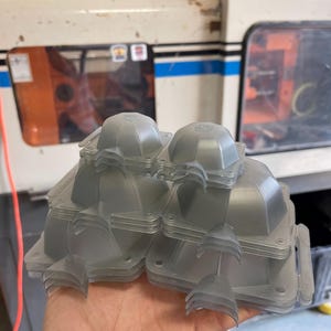 May include: A stack of clear plastic molds, likely for injection molding, with a rounded top and a flat base. The molds are stacked in a pyramid shape.