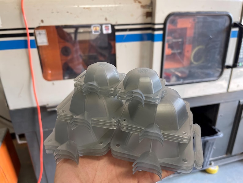 May include: A stack of clear plastic molds, likely for injection molding, with a rounded top and a flat base. The molds are stacked in a pyramid shape.