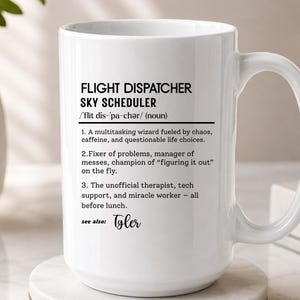 May include: A white ceramic mug featuring black printed text that defines a flight dispatcher as a sky scheduler, a multitasking wizard fueled by chaos and caffeine, a fixer of problems, and an unofficial therapist, with the name Tyler listed below.