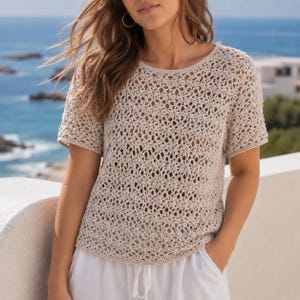 Puede incluir: Una blusa de crochet beige de manga corta con un intrincado patrón floral de punto abierto, cuello redondo y dobladillo recto. La prenda está confeccionada con hilo ligero y texturizado, mostrando un diseño semitransparente en todo el cuerpo.