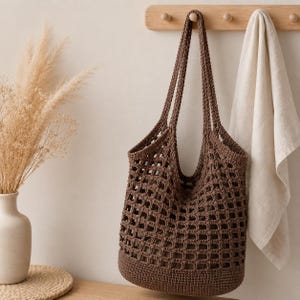 May include: A dark brown crochet tote bag featuring a square grid pattern throughout the body, a solid base, and two long shoulder straps. The bag is constructed with a dense, textured yarn and has an open-weave design that reveals a solid inner lining.