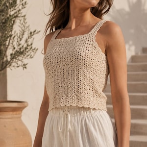Può includere: Un top smanicato all'uncinetto color beige con scollo quadrato e orlo smerlato. Il capo è realizzato con un motivo traforato e spalline larghe, abbinato a pantaloni bianchi con coulisse in tessuto leggero.