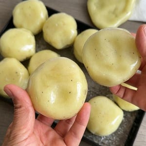 Peut inclure: Plusieurs aliments ronds, jaune pâle, translucides et à la texture lisse, parsemés de petits points sombres. Chaque pièce a un aspect brillant et ferme, disposée sur un plateau sombre, avec deux pièces tenues pour être présentées.
