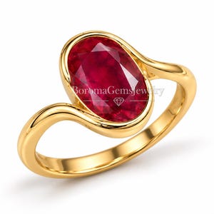 Puede incluir: Un anillo de oro con una gran piedra preciosa de color rojo intenso y corte ovalado en un engaste de bisel liso. La banda tiene un diseño curvo y ondulado que fluye hacia el engaste. El texto BoromaGemsJewelry es visible sobre la piedra roja.