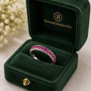 Peut inclure: Une bague en argent ornée d'une rangée de rubis ronds d'un rouge rosé vif sertis dans un canal. La bague est présentée dans un écrin à bijoux en velours vert foncé avec le texte doré BoromaGemsJewelry imprimé sur le couvercle intérieur.