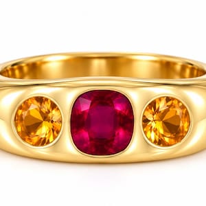 Op de afbeelding: Een gepolijste geelgouden ring met een centrale kussengeslepen dieprode robijn, geflankeerd door twee rondgeslepen levendige oranje citrienen. De stenen zijn verzonken in het gladde, afgeronde oppervlak van de dikke, massief gouden ringband.