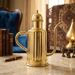 Puede incluir: Una aceitera de latón pulido con un cuerpo cilíndrico de estrías verticales, un pico curvo y una tapa abovedada con un pequeño remate esférico. El recipiente de metal cuenta con un asa resistente en el lateral y una base circular.