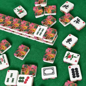 May include: A set of mahjong tiles featuring white faces with black and green traditional symbols and backs decorated with a vibrant pattern of monkeys, yellow umbrellas, pink flowers, and green tropical leaves on a pink background.