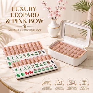 May include: A Mahjong set featuring tiles with leopard print backs and green, red, and black character designs. The set includes a white quilted travel case with a clear lid and gold zipper, displayed alongside rows of tiles on a marble surface.