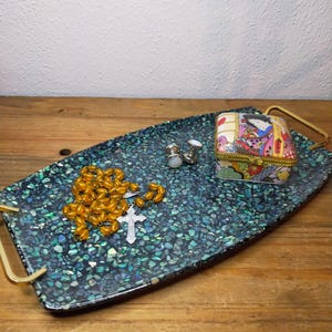 May include: A rectangular serving tray with gold-tone handles, featuring a dark green and blue iridescent mosaic surface. On the tray sits a string of amber-colored beads with a silver cross, two silver cufflinks, and a small rectangular trinket box.