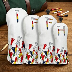 Könnte beinhalten: Ein Set aus vier weißen Golfschlägerhauben mit einem Muster aus roten, gelben und blauen Golftees am unteren Rand. Die Hauben zeigen die Buchstaben I, F, F und H, die aus Golftees in denselben Farben gebildet sind, jeweils mit einer schwarzen Zuglasche.