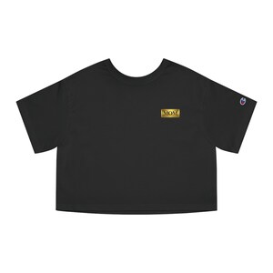 Op de afbeelding: Zwart cropped T-shirt met een gouden rechthoekige patch met de tekst "MOM". Het shirt heeft korte mouwen en een ronde hals. Een klein Champion-logo is zichtbaar op de linkermouw.
