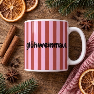 Könnte beinhalten: Ein weißer Keramikbecher mit vertikalen Streifen in abwechselnden Tönen von Hellrosa und Dunkelrot. Der Text glühweinmaus. ist in schwarzen, kleingeschriebenen, serifenlosen Buchstaben in der Mitte des Bechers aufgedruckt, der einen geschwungenen Henkel hat.