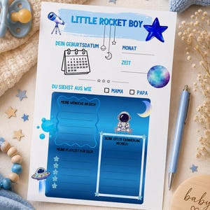 Könnte beinhalten: Ein Baby-Erinnerungsbuch mit blauem und weißem Design, mit dem Text "Little Rocket Boy". Das Buch enthält Abschnitte zum Aufzeichnen von Geburtsdaten, Wünschen und Erinnerungen. Dekorative Elemente sind Sterne, Mond und Astronaut.