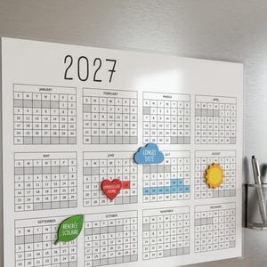 Peut inclure: Un calendrier mural magnétique blanc pour l'année 2027 avec des lignes et du texte noirs, incluant des aimants colorés en forme de nuage bleu, cœur rouge, soleil jaune et feuille verte, avec un porte-stylo en maille argentée et deux marqueurs.