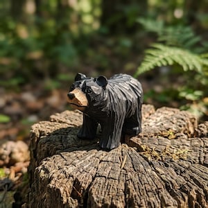 Pode incluir: Uma pequena estatueta de madeira esculpida à mão de um urso preto com um focinho castanho claro. O urso tem um acabamento de superfície texturizado e facetado, e é representado em pé, exibindo marcas de cinzel visíveis no corpo escuro.