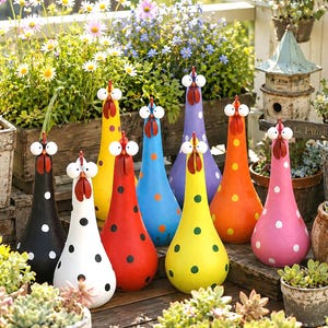 Può includere: Una collezione di otto statuette di gallina a forma di goccia in vari colori, tra cui nero, bianco, giallo, rosso, blu, viola, arancione e rosa. Ogni gallina presenta pois bianchi, grandi occhi rotondi e cresta e bargigli rossi.