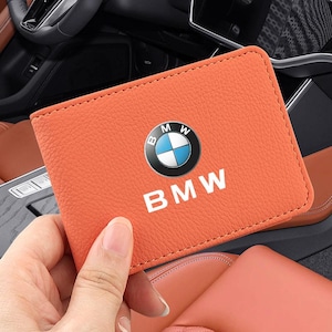 Peut inclure: Un portefeuille rectangulaire orange à la surface texturée, orné du logo BMW et du texte blanc BMW imprimé en dessous. Le portefeuille présente des coutures visibles sur les bords et offre un design classique et fonctionnel.