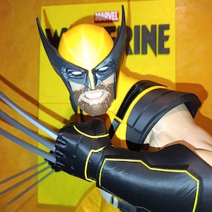 Può includere: Un action figure di Wolverine che indossa una tuta gialla e nera con maschera abbinata, caratterizzata da una barba castana e denti scoperti. Il personaggio ha artigli d'argento estesi su una mano ed è posizionato davanti a un cartello giallo Marvel Wolverine.