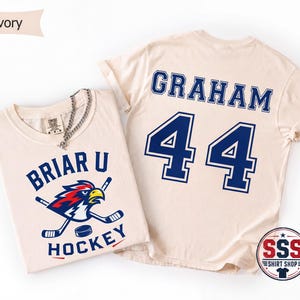 May include: Two ivory t-shirts. The front features a graphic of a bird mascot with hockey sticks and the text BRIAR U HOCKEY. The back displays the name GRAHAM and the number 44 in large blue block lettering with a dark blue outline.