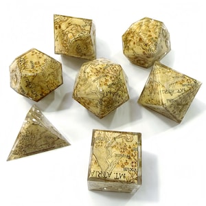 May include: A set of seven polyhedral dice made of clear resin with an embedded vintage map design featuring brown ink lines, topographical markings, and text labels such as Mt. Atria, The Tumb, and Aveléon visible on the various geometric shapes.