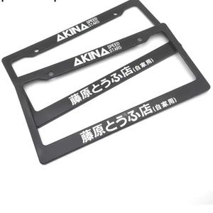 Könnte beinhalten: Zwei schwarze rechteckige Kennzeichenhalter. Der obere Rahmen zeigt den weißen Schriftzug AKINA SPEED STARS. Der untere Rahmen zeigt den weißen japanischen Text 藤原とうふ店 (自家用). Beide Rahmen verfügen über vorgebohrte Montagelöcher.