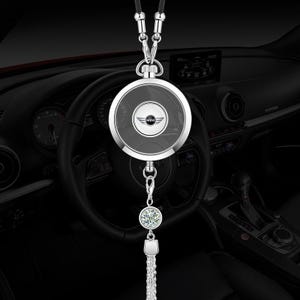 May include: A silver-toned car rearview mirror hanging ornament featuring a circular frame with a central MINI logo emblem. The accessory includes a dangling silver chain, a single round clear crystal charm, and a metallic tassel at the bottom.