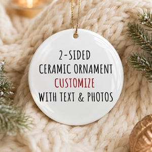 May include: A round white ceramic ornament featuring a gold hanging string. The front surface displays black text that reads 2-SIDED CERAMIC ORNAMENT, followed by the word CUSTOMIZE in red, and the text WITH TEXT & PHOTOS in black below it.