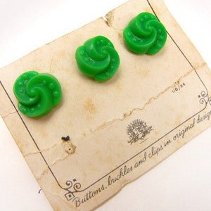 May include: Three green swirl buttons with a white background. The buttons are on a card that says "Buttons, buckles and clips in original designs".