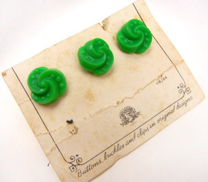 May include: Three green swirl buttons with a white background. The buttons are on a card that says "Buttons, buckles and clips in original designs".