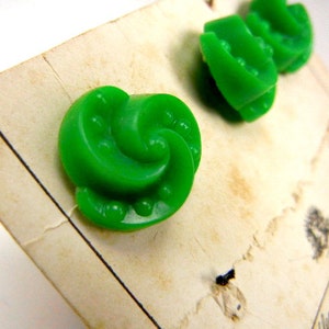 May include: Three green plastic buttons with a swirl design and small white dots. The buttons are on a white card.