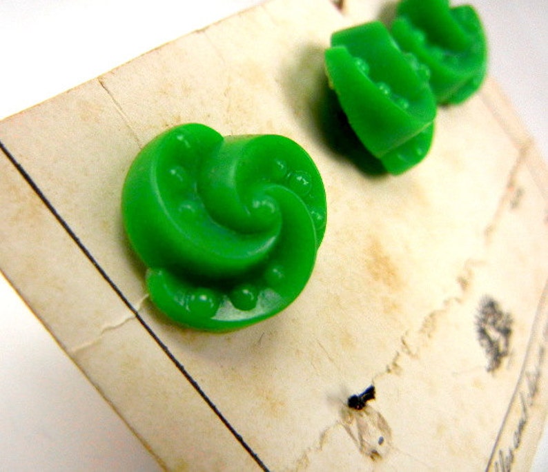 May include: Three green plastic buttons with a swirl design and small white dots. The buttons are on a white card.