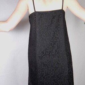 May include: A black lace dress with thin straps. The dress has a fitted bodice and a slightly flared skirt.