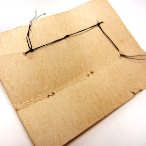 May include: A close-up of the back of a brown cardboard card with black string tied through holes in the corners.