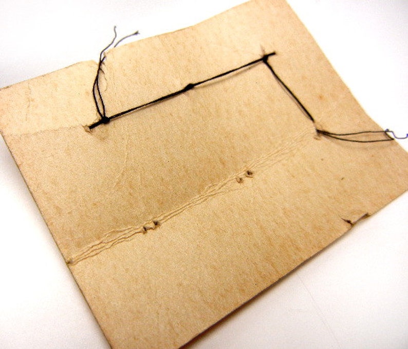 May include: A close-up of the back of a brown cardboard card with black string tied through holes in the corners.