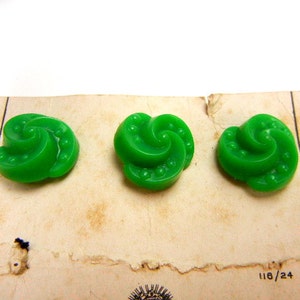 May include: Three green plastic buttons with a swirl design. The buttons are on a white card with the number 118/24 printed on it.