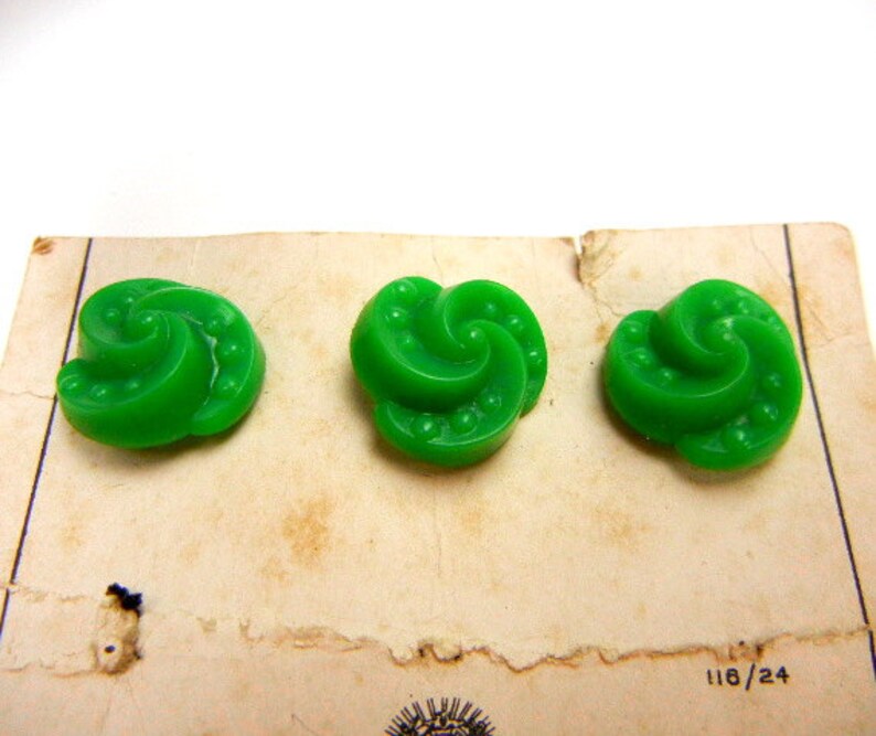 May include: Three green plastic buttons with a swirl design. The buttons are on a white card with the number 118/24 printed on it.