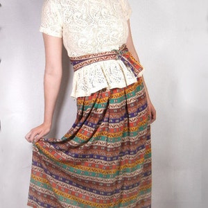 May include: A woman wearing a white lace top with a colorful patterned skirt and black heels.